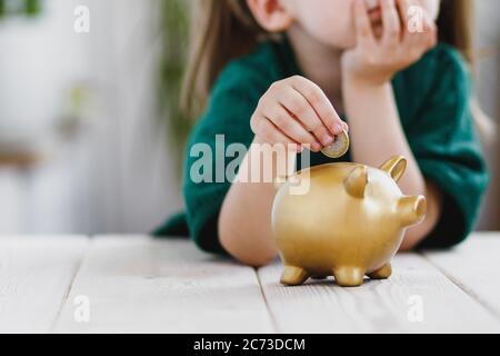 Kleines Mädchen in grünem Kleid denken über ihr Geld ausgeben und eine Münze in ein Sparschwein. Sparkonzept Stockfoto