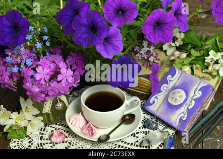 Tasse Tee mit Petunia Blumen und Bücher auf dem Tisch. Esoterischer, gotischer und okkulter Hintergrund mit magischen Objekten, mystischem und Märchenkonzept Stockfoto