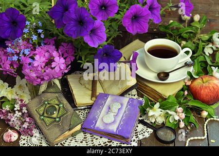 Romantisches Stillleben mit Petunia-Bouquet, dekorierten Tagebuch und Tasse Tee. Esoterischer, gotischer und okkulter Hintergrund mit magischen Objekten, Mystiker und Fee Stockfoto