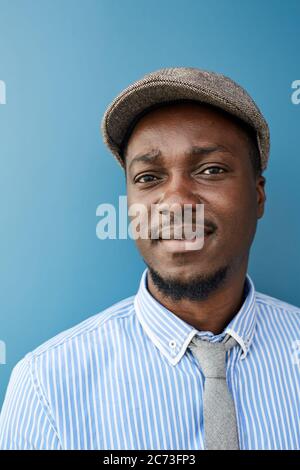 Porträt eines afrikanischen jungen Geschäftsmannes in Mütze Blick auf die Kamera, während sie vor dem blauen Hintergrund Stockfoto