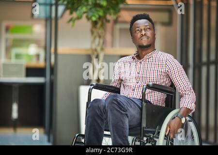 Afrikanischer behinderter Büroangestellter sitzt im Rollstuhl er ist im Bürogebäude Stockfoto