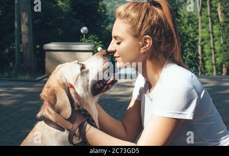 Seitenansicht Foto einer blonden Dame küssen ihre goldene Retriever im Park in der Sonne Stockfoto