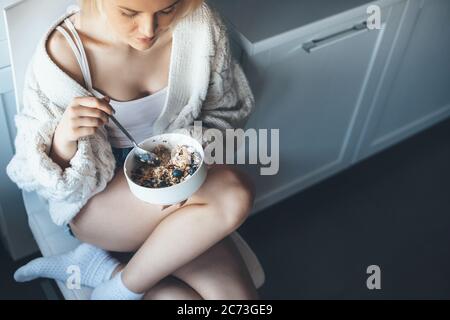 Foto von oben einer blonden Dame in der Küche, die Getreide isst und Strickpullover auf dem Boden trägt Stockfoto