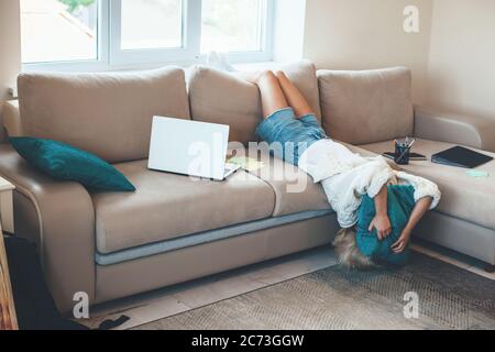 Erschöpft kaukasischen blonde Frau auf der Couch liegen, während die Arbeit am Laptop mit einigen Ordnern Stockfoto