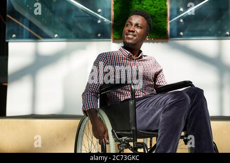 Afrikanischer Mann im Rollstuhl, der wegschaute und lächelte in ein modernes Büro Stockfoto