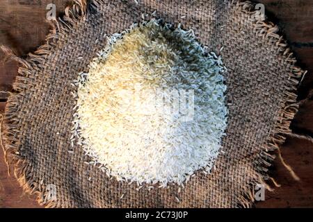Reis aus einem kleinen Sack isoliert auf Holzgrund. Frischer Reis im Sack auf Holz strukturiertem Hintergrund. Nahaufnahme von rohem Reiskorn auf Sacktuch. Stockfoto