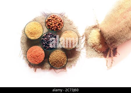 Reis aus einem kleinen Sack isoliert auf weißem Hintergrund. Verschiedene bunte Puls in Schalen. Küken Erbsengewächses, Rote Niere, Linsen, Fenckshornkleesamen, Weizendalie, Stockfoto