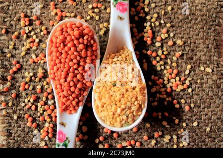 Haufen ungekochte rote Linsen und Taubenerde. Mungbohnen und rote Linsen in zwei Löffeln isoliert auf Sack strukturierten Hintergrund. Stockfoto