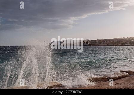 Am späten Nachmittag erhellt die Sonne die brechende Welle am Hananya Beach am Golf von Eilat mit niedrigen Wolken oben und der Urlaubsstadt eilat im Hintergrund Stockfoto