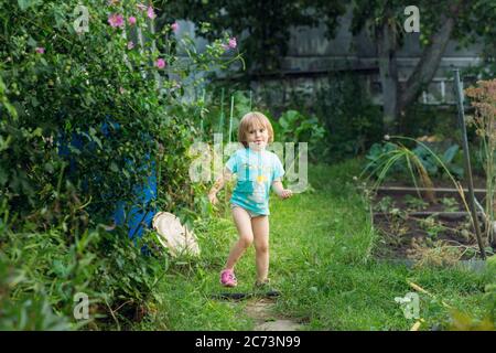 Kleines Mädchen in einem blauen T-Shirt macht Gesichter im Garten. Stockfoto