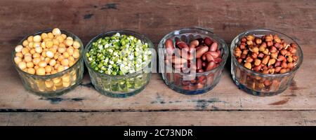 Sammlung von Hülsenfrüchten (Kichererbsen, grüne Erbsen, grüne Mungbohnen, rote Niere, trockene Erbsen)in verschiedenen Schüsseln isoliert auf Holzgrund. Stockfoto