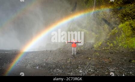 Skogar, Island - Mai 2019: Mann steht unter dem Regenbogen im Skogafoss Wasserfallgebiet Stockfoto