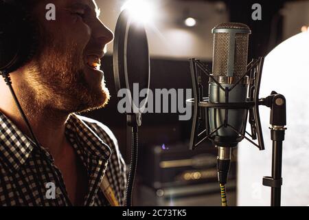 Professionelle kaukasischen Sänger Mann singen im Aufnahmestudio. Schöner Kerl genießen Sie die Durchführung von Musik, emotionale Sänger mit Mikrofon und Headset Stockfoto