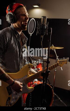 Junge kaukasische Profi-Gitarrist singen am Mikrofon und Gitarre gleichzeitig spielen. Musik, Rock and Roll Konzept Stockfoto