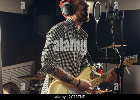 Junge kaukasische Profi-Gitarrist singen am Mikrofon und Gitarre gleichzeitig spielen. Musik, Rock and Roll Konzept Stockfoto