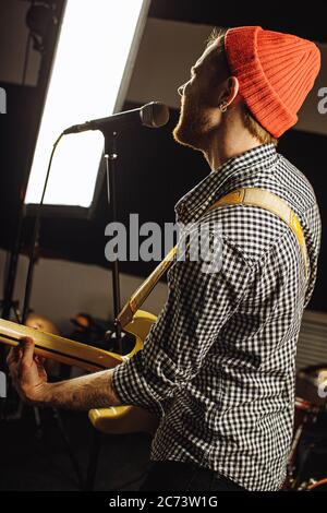 Junge kaukasische Profi-Gitarrist singen am Mikrofon und Gitarre gleichzeitig spielen. Musik, Rock and Roll Konzept Stockfoto