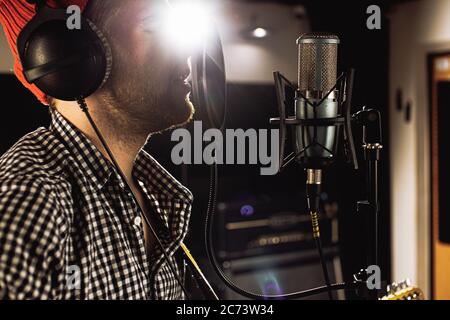 Seitenansicht auf kaukasischen jungen Mann singen auf Mikrofon im Aufnahmestudio. Schöner Kerl führen Musik, Tragen von Headsets. Musikkonzept Stockfoto