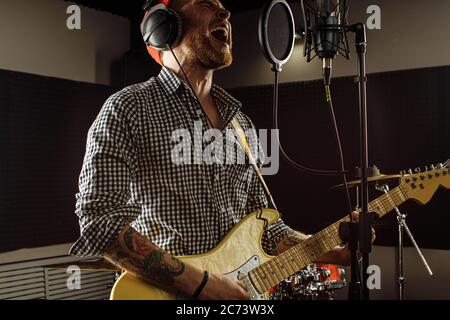 Professionelle kaukasische Sänger spielen E-Gitarre in Aufnahmestudio. Mann scharf auf Rock und Roll, genießen Sie die Durchführung von Musik. Musik, Instrumente Konzept Stockfoto