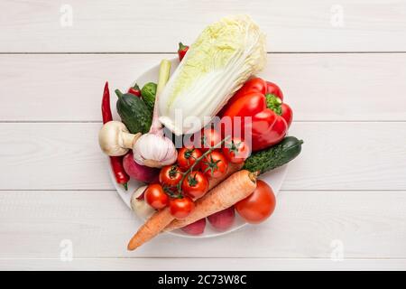 Verschiedene rohe Gemüse auf einem weißen Teller und Holzhintergrund mit leeren Raum um. Zucchini, Gurke, Chili, Pilze, Tomaten, Blumenkohl Stockfoto