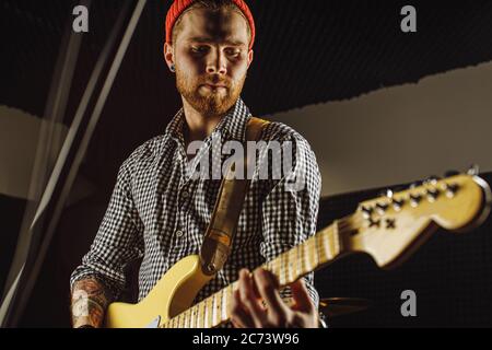 Junge kaukasische Rockmusiker spielen auf E-Gitarre, Mann scharf auf Rockmusik, führen Musik im Aufnahmestudio. Instrumente, Ausrüstung, Musik concep Stockfoto