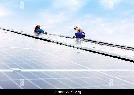 Elektroingenieure mans arbeiten daran, Sonnenkollektoren auf Solarstation auf dem Dach gegen blauen Himmel zu installieren. Entwicklung von Sun alternative Energietechnologie Stockfoto