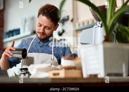 Schöner Barista für Erwachsene mit stilvollem Bart, macht gemahlenen Kaffee hinter Holztheke, in modernem Café, von unten geschossen Stockfoto