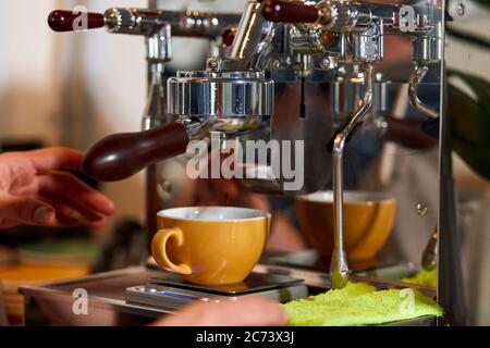 Schöne gelbe Kaffeetasse steht auf Kaffeemaschine, Hände der männlichen Barista ist bereit, große Tasse von americano, Kaffeehaus Konzept zu nehmen Stockfoto