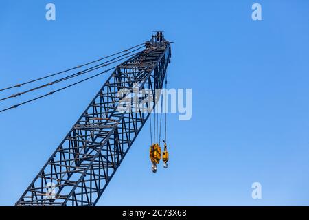 Große Takelage Kran Closeup Arm verlängerte Sektion mit Stahlseilen und zwei gelben Haken Industriebau mechanische Ausrüstung in blauen Himmel. Stockfoto