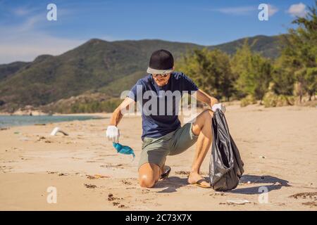 Mann in Handschuhen holt Plastikbeutel, die das Meer verschmutzen. Problem mit verschütteten Müll Müll Müll Müll Müll auf dem Strand Sand durch von Menschen verursachte Verschmutzung und Stockfoto