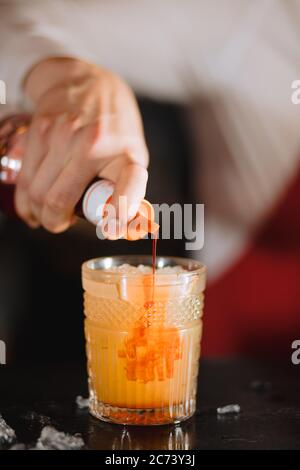 Der Barkeeper gießt Sirup in exotischen Fruchtcocktail, exotischer Fruchtcocktail in Glas isoliert auf verschwommenem Restauranthintergrund, Nahaufnahme Stockfoto