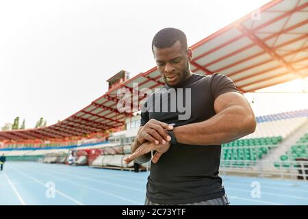 Schöner starker Mann, der beim Training im Stadion auf die Smartwatch schaut. Er ist zufrieden mit den Ergebnissen.Nahaufnahme Porträt. Stockfoto