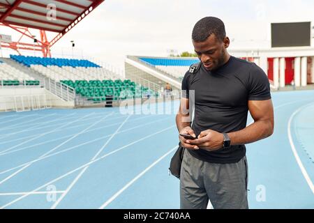 Gut aussehend lächelnden Sportler mit Handy im Stadion, Nahaufnahme Porträt, Kopierer Raum. Gadget, Technologie Stockfoto