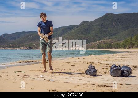 Mann in Handschuhen holt Plastikbeutel, die das Meer verschmutzen. Problem mit verschütteten Müll Müll Müll Müll Müll auf dem Strand Sand durch von Menschen verursachte Verschmutzung und Stockfoto