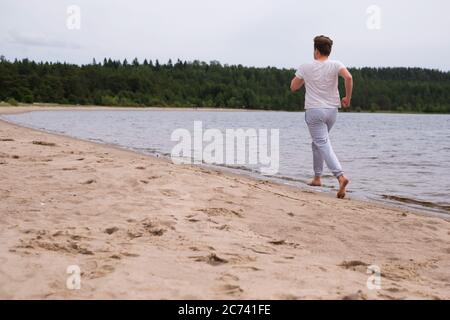 Junger Kaukasischer in Fitnesskleidung am Sandstrand entlang. Rückansicht Stockfoto