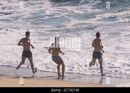 Männliche Urlauber, die sich in einem Aufenthalturlaub am Fistral Beach in Newquay in Cornwall ins Meer blicken lassen. Stockfoto