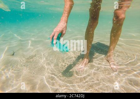 Der Mensch sammelt Pakete aus dem wunderschönen türkisfarbenen Meer. Paradies Strand Verschmutzung. Problem mit verschütteten Müll Müll Müll Müll Müll auf dem Strand Sand verursacht durch Stockfoto