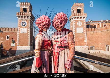 VENEDIG, ITALIEN - 28. FEBRUAR 2020: Zwei rosa und blumige Masken posieren vor dem Arsenale von Venedig während des Karnevals von Venedig Stockfoto