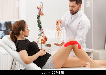 Kinesiologie Taping.Physikalischer Therapeut Anwendung von Kinesiologieband auf den Patienten Knie.Therapeut Behandlung verletzter Knie des jungen Athleten.Post traumatisch Stockfoto