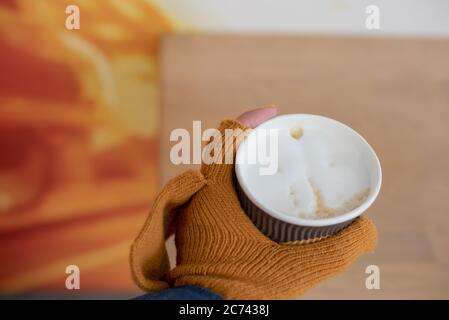 Heißes Getränk in einem Becher in den Händen mit Handschuhen auf Nahaufnahme. Eine Papiertasse mit Kaffee in der Hand in Handschuhen. Stockfoto