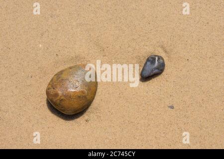 Zwei glatte Strandkiesel vor einem Hintergrund aus flachem, wassergewaschenen Sand Stockfoto