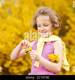 Lächelndes Mädchen macht einen Kranz aus Löwenzahn im Frühling im Garten Stockfoto