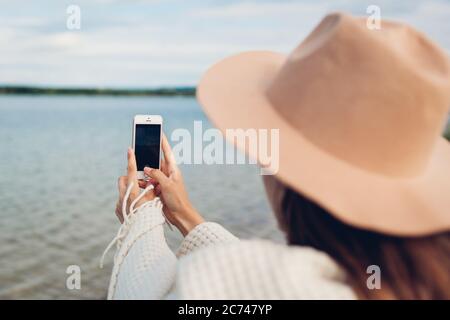 Frau Tourist fotografieren Herbst See ladscape mit Smartphone. Reisende in Hut mit Decke bedeckt Stockfoto