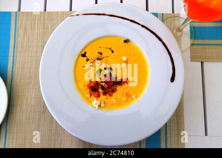 Hellgelbe Maiscremesuppe, garniert mit Gemüse in weißem Teller steht auf einer Bambusmatte. Köstliche vegetarische Speisen, ein Gericht mit Gemüse und Stockfoto