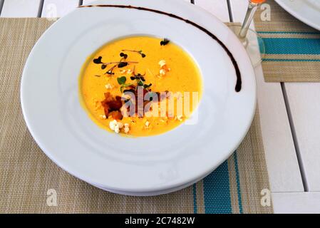 Hellgelbe Maiscremesuppe, garniert mit Gemüse und Kräutern in weißem Teller steht auf einer Bambusmatte. Leckeres vegetarisches Essen, ein Gericht Stockfoto