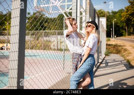 Cool Kerl stehen mit schönen Mädchen und Ordnung in seine Haare, während sie träumerisch beiseite schauen. Mädchen in Jeans und Spitzenmütze verbringen Zeit mit Jungen auf Stockfoto