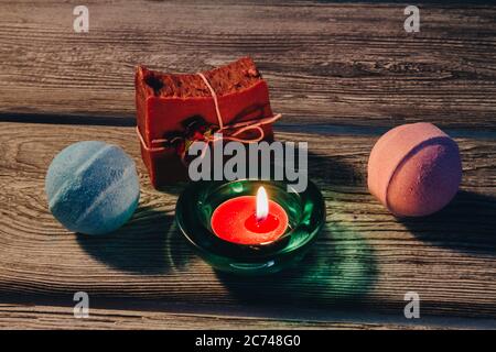 Spa-Konzept mit Badbomben, handgefertigter Seife und brennender Kerze auf Holzhintergrund. Stockfoto