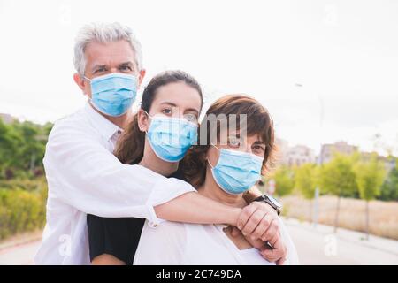 Neue normale. Maskierte Familienumarmungen. Die Mitglieder einer Familie umarmen sich mit Schutzmasken. Familie geschützt mit Masken gegen Coronavirus. Sicherheit und Stockfoto