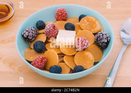 Nahaufnahme der blauen Schüssel mit Müsli-Pfannkuchen und Himbeeren, Heidelbeeren und Brombeeren mit Butter gefüllt Stockfoto