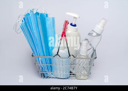 Supermarkt-Korb mit schützender medizinischer Maske und eine Flasche Alkohol Handgel Desinfektionsmittel. Coronavirus Shopping-Konzept auf hellgrauem Hintergrund Stockfoto