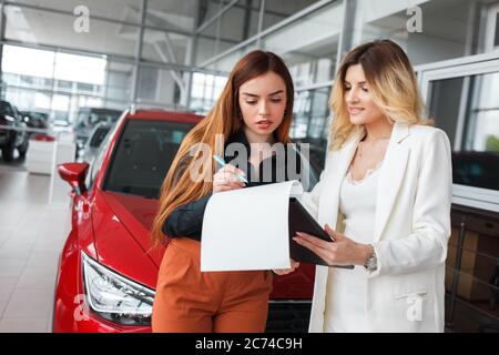 Verkäuferin des Autohauses gibt Dokumente für die Unterzeichnung für eine weibliche Kundin Stockfoto